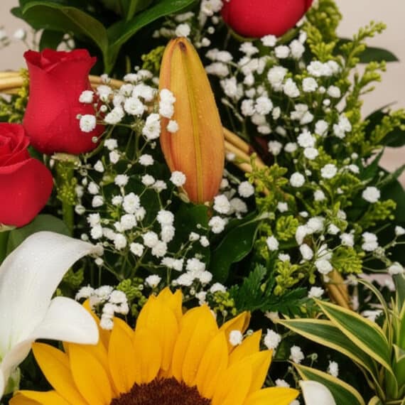 Primer plano extremo de un arreglo floral Capella con rosas rojas, lirios blancos, girasoles amarillos y pequeñas flores blan