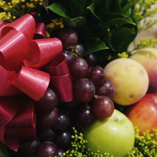 Primer plano extremo de un arreglo floral con frutas salak, uvas rojas, manzanas verdes y duraznos, destacando texturas y got