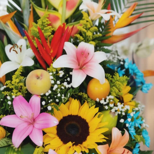 Primer plano extremo de Arreglo Floral con Frutas Tentación, mostrando lirios rosados y blancos, girasoles, aves del paraíso,