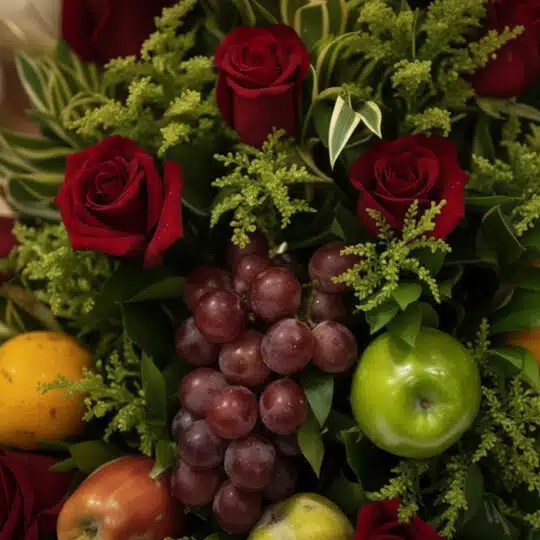 Primer plano extremo de un arreglo floral con rosas rojas vibrantes, uvas rojas, una manzana verde brillante y otras frutas t