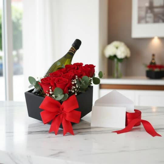 Arreglo floral NATALE con rosas rojas vibrantes, una botella de vino, tarjeta de regalo elegante y cinta roja sobre mármol.