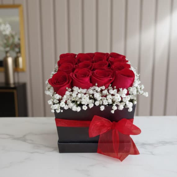Arreglo floral Pétalos con rosas rojas frescas y gypsophila en una caja negra con lazo rojo, sobre mármol blanco en un entorn
