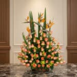 Arreglo floral grande con rosas color salmón y aves del paraíso, sobre una mesa de mármol en un entorno elegante de hotel bou