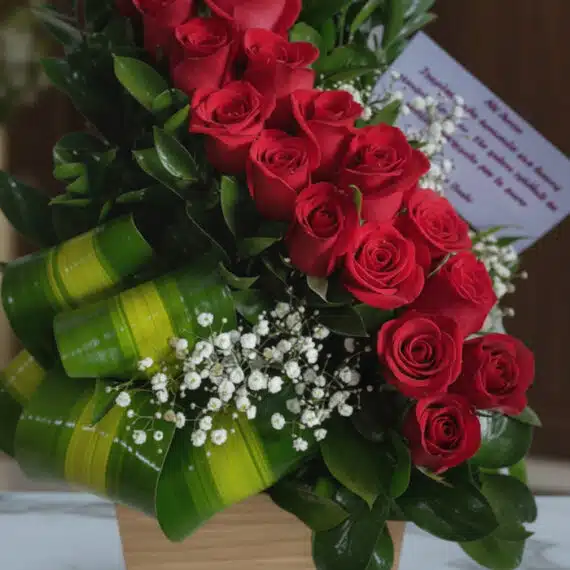 Primer plano extremo de un arreglo floral con rosas rojas espiral, gotas de rocío sutiles y hojas verdes vibrantes, destacand