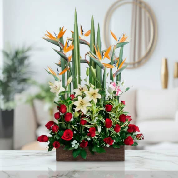 Arreglo Floral Siempre Juntos: Elegancia Tropical para Momentos Especiales Arreglo floral 'Siempre Juntos' con aves del paraíso, lirios blancos y rosas rojas en base de madera, sobre mármol.