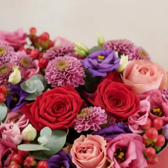 Primer plano extremo del Arreglo Floral ZITA, mostrando rosas rojas y rosadas, lisianthus morados, crisantemos púrpuras y bay