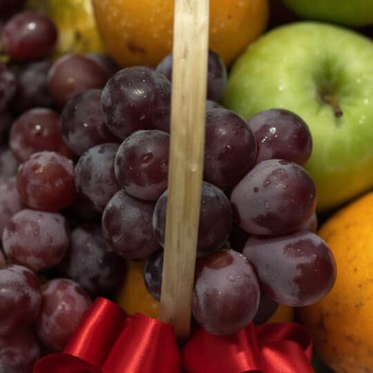 Primer plano extremo de uvas rojas frescas con gotas de rocío, parte de una canasta de frutas premium, con una manzana verde