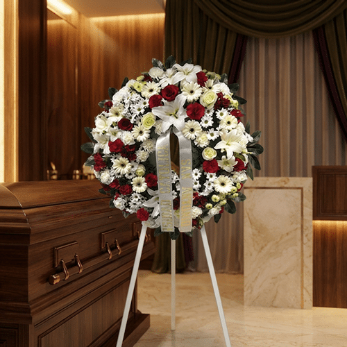 Corona de flores fúnebres Ararat con rosas rojas, lirios blancos y margaritas, junto a un ataúd de madera en un ambiente eleg