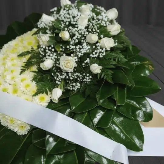 Fotografía macro premium de la Corona Fúnebre Descansa en Paz, mostrando texturas hiperrealistas de pétalos blancos y follaje