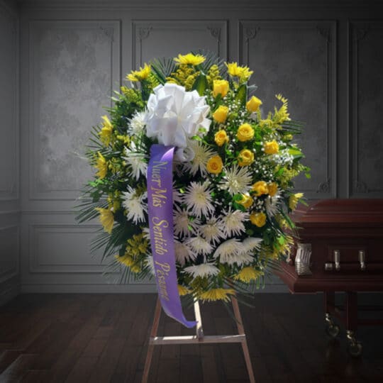 Corona fúnebre 'Estamos Contigo' con flores amarillas y blancas, cinta morada con mensaje de condolencia, junto a un ataúd en