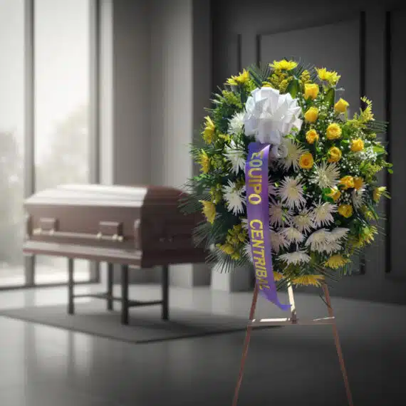 Corona fúnebre 'Estamos Contigo' con flores amarillas y blancas, cinta morada, en sala de velación moderna con ataúd desenfoc