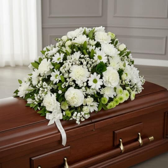 Cubre caja fúnebre Epifania con flores blancas y cinta de condolencia, vista desde un ángulo diferente y composición renovada