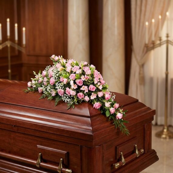 Cubre Caja Fúnebre en Homenaje a Juana con Rosas Rosadas Cubre caja fúnebre elegante con rosas rosadas y follaje verde, delicadamente dispuesto sobre un ataúd de madera oscura en un