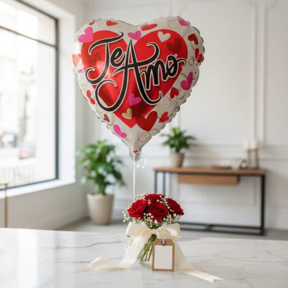 Globo metalizado en forma de corazón con la frase 'Te Amo' flotando sobre un arreglo de rosas rojas frescas en un jarrón de c