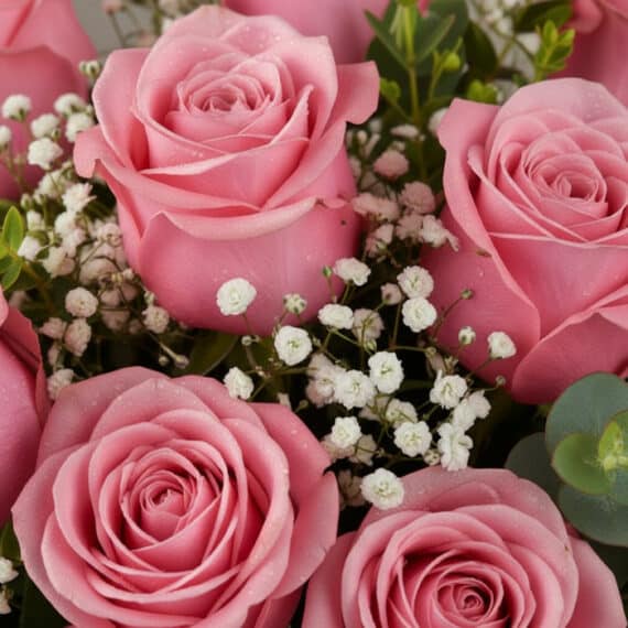 Primer plano extremo de un ramillete de rosas rosadas frescas con gotas de rocío, gypsophila y hojas verdes, bajo luz natural